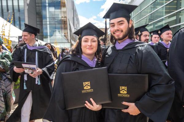 Two students from the School of Architecture and Design pose with their diplomas in their caps and gowns at graduation