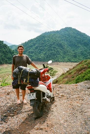 A man leaning on a bike on a dirt road