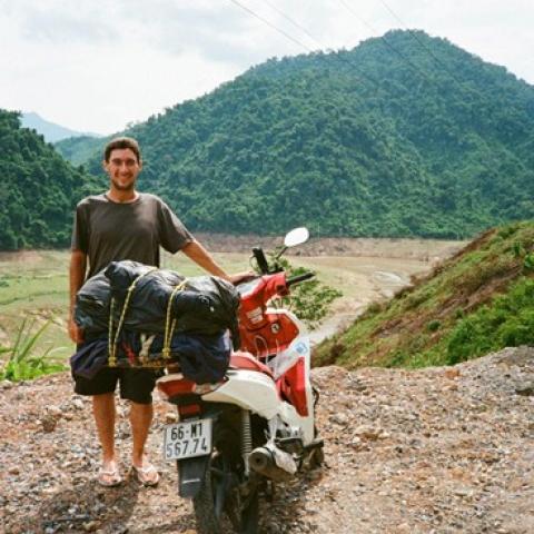 A man leaning on a bike on a dirt road